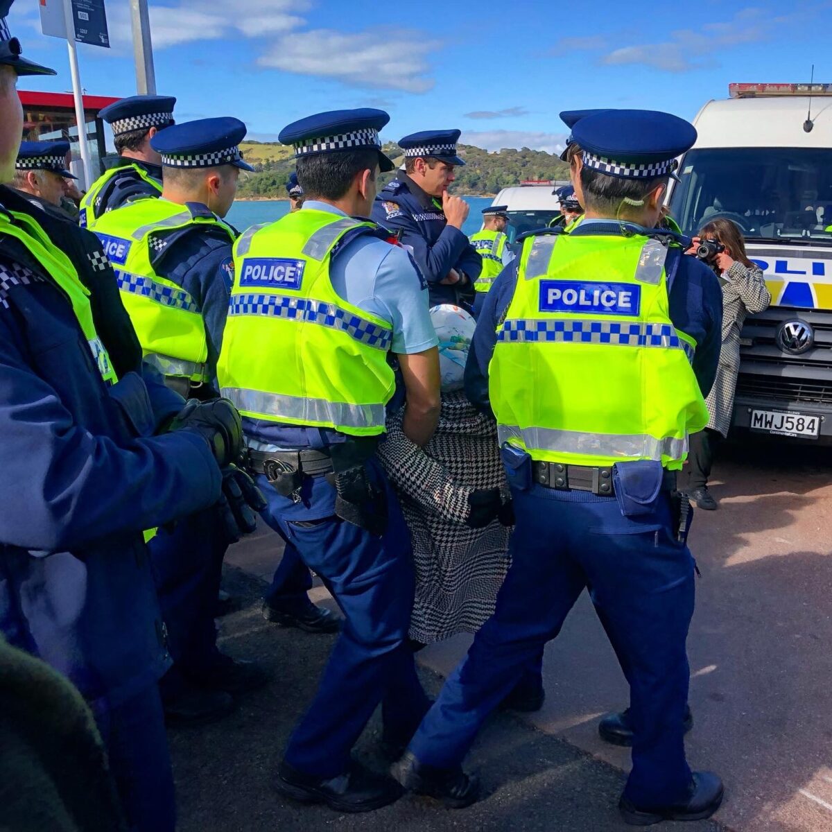 Yeni Zelanda polisi, Waiheke Adası’ndaki Pūtiki koyunda yer alan Kennedy Point Körfezi’nde bir protestocuyu uzaklaştırırken, o anları Waiheke Gulf News adlı yerel gazetede muhabirlik yapan Erin Johnson fotoğraflıyor. (Fotoğraf: Wikimedia)