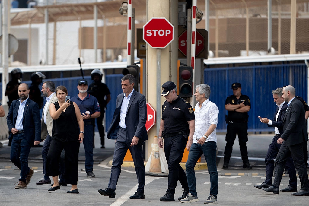 İspanya, İtalya ile göç anlaşmazlığı sonrası yolculara geçici sınır kontrolleri uygulamaya başladı. İspanya Başbakanı Pedro Sánchez (ortada sol) ile İçişleri Bakanı Fernando Grande-Marlaska (ortada sağ), Ceuta’daki Tarajal sınır çitinin yanında yürüyor. İki yetkili, 31 Temmuz 2026’da Fas’tan binlerce göçmenin gece boyunca geçiş yaptığı sırada, sınırdaki göç krizini yönetmek amacıyla bölgeyi ziyaret etti. (Fotoğraf: Jorge Guerrero, AFP - Getty Images, The Epoch Times aracılığıyla)